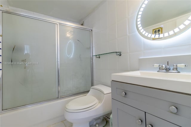 full bathroom with combined bath / shower with glass door, tile walls, tile patterned flooring, toilet, and vanity