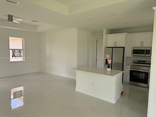 kitchen with light tile patterned floors, appliances with stainless steel finishes, a center island, ceiling fan, and white cabinets