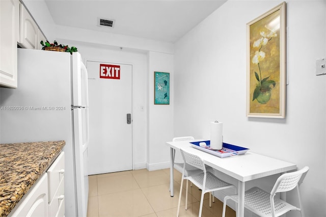 kitchen featuring white cabinetry, white refrigerator, light stone counters, and light tile patterned flooring