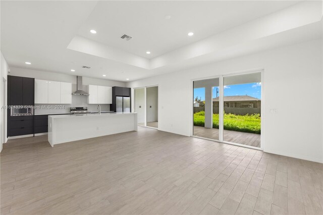 unfurnished living room with a raised ceiling, sink, and light wood-type flooring