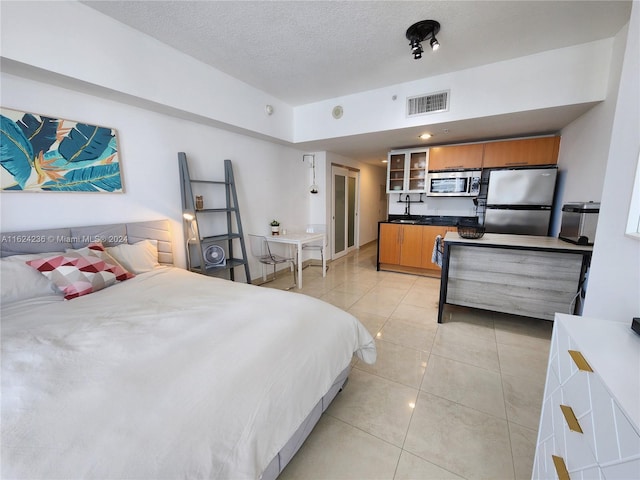 bedroom with sink, a textured ceiling, stainless steel refrigerator, and light tile patterned flooring