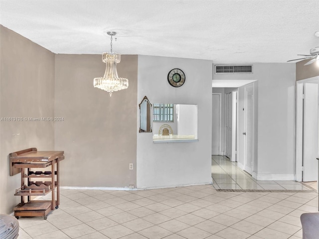 tiled empty room featuring ceiling fan with notable chandelier and a textured ceiling