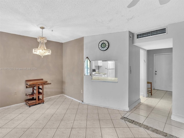 spare room with light tile patterned floors, ceiling fan with notable chandelier, and a textured ceiling