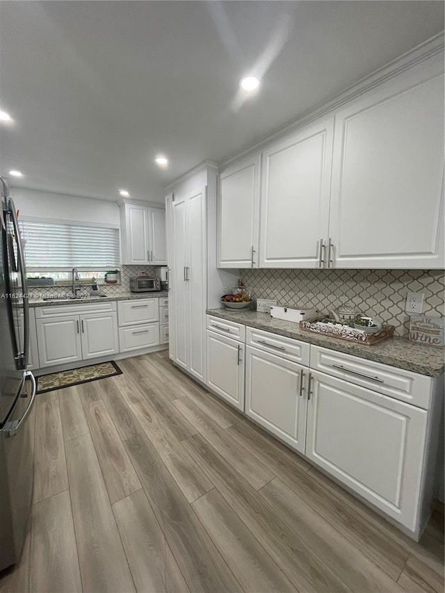 kitchen with white cabinetry, light hardwood / wood-style flooring, fridge, decorative backsplash, and sink