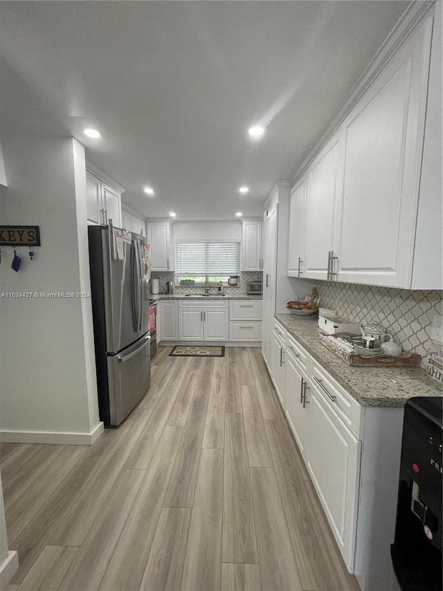 kitchen with stainless steel refrigerator, white cabinets, light stone counters, light hardwood / wood-style floors, and sink