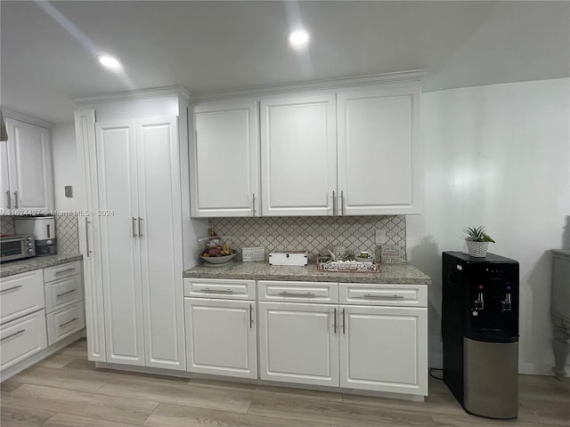 kitchen with white cabinetry, stone countertops, light wood-type flooring, and backsplash