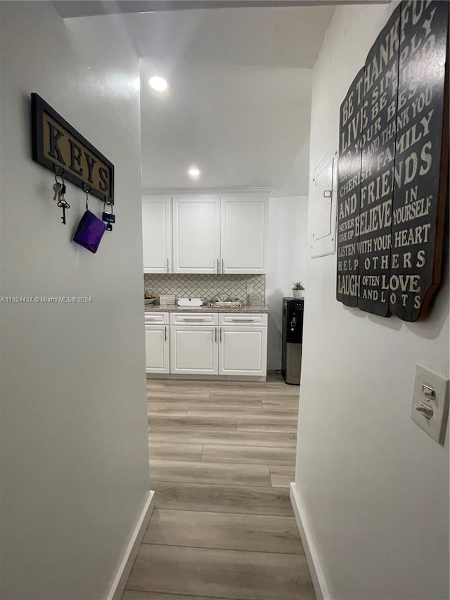 kitchen with white cabinets, electric panel, light hardwood / wood-style flooring, and tasteful backsplash