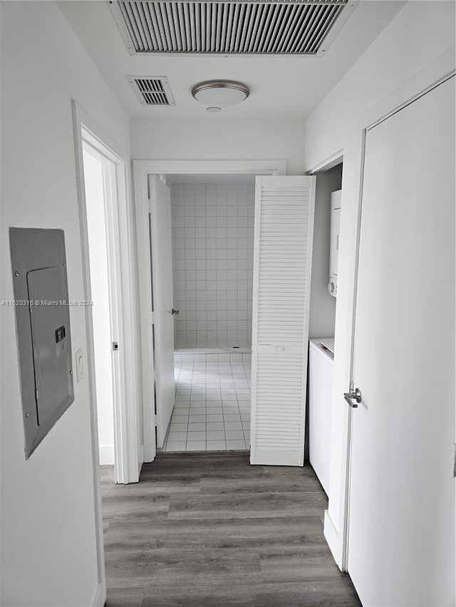 hallway featuring stacked washing maching and dryer, dark hardwood / wood-style flooring, and electric panel