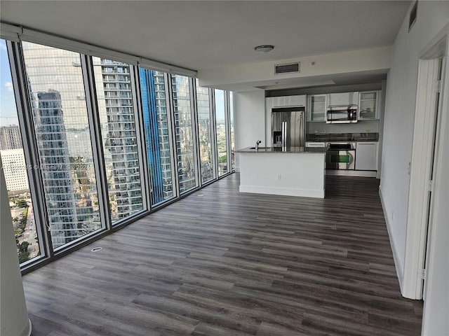 kitchen with stainless steel appliances, white cabinets, a wall of windows, and dark wood-type flooring