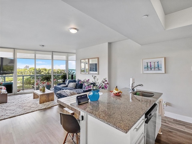 kitchen with floor to ceiling windows, sink, white cabinetry, stone countertops, and dishwasher