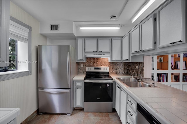 kitchen featuring stainless steel appliances, gray cabinetry, sink, backsplash, and light tile patterned floors