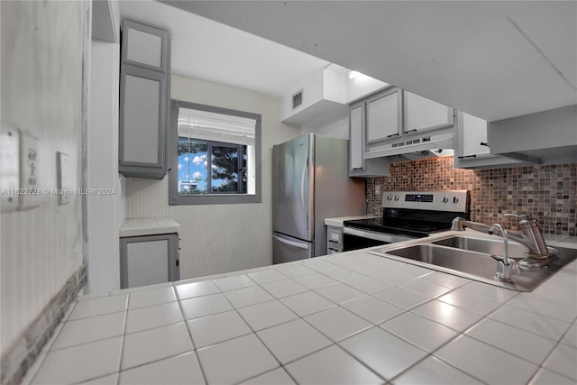 kitchen featuring stainless steel appliances, decorative backsplash, tile countertops, sink, and gray cabinetry