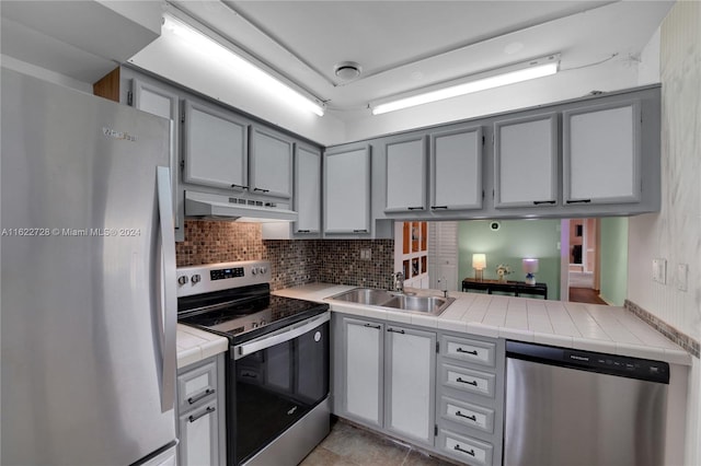 kitchen featuring gray cabinets, light tile patterned flooring, stainless steel appliances, decorative backsplash, and sink