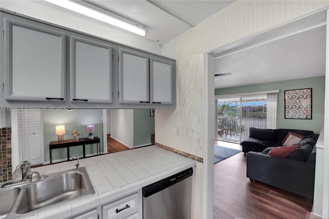 kitchen with gray cabinetry, sink, tile counters, dishwasher, and dark wood-type flooring