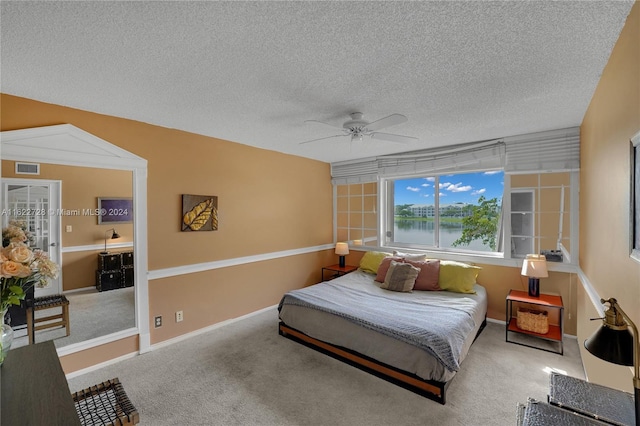 bedroom with carpet floors, a water view, a textured ceiling, and ceiling fan