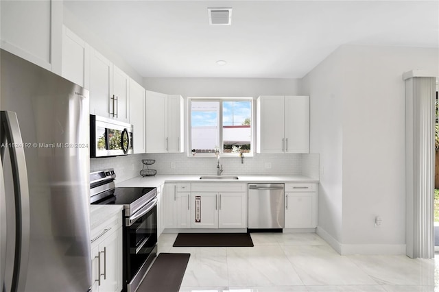 kitchen with appliances with stainless steel finishes, sink, backsplash, light tile patterned floors, and white cabinetry