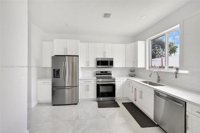 kitchen featuring light tile patterned flooring, white cabinetry, stainless steel appliances, decorative backsplash, and sink