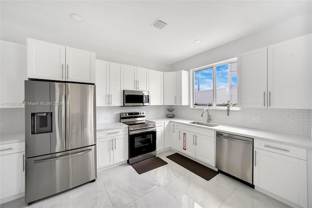 kitchen with appliances with stainless steel finishes, white cabinets, sink, backsplash, and light tile patterned floors