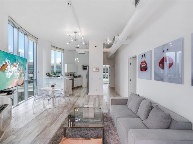 living room with a healthy amount of sunlight, a towering ceiling, light wood-type flooring, and a chandelier