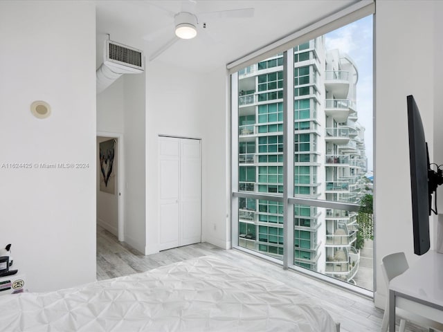bedroom with light wood-type flooring, expansive windows, ceiling fan, and a closet