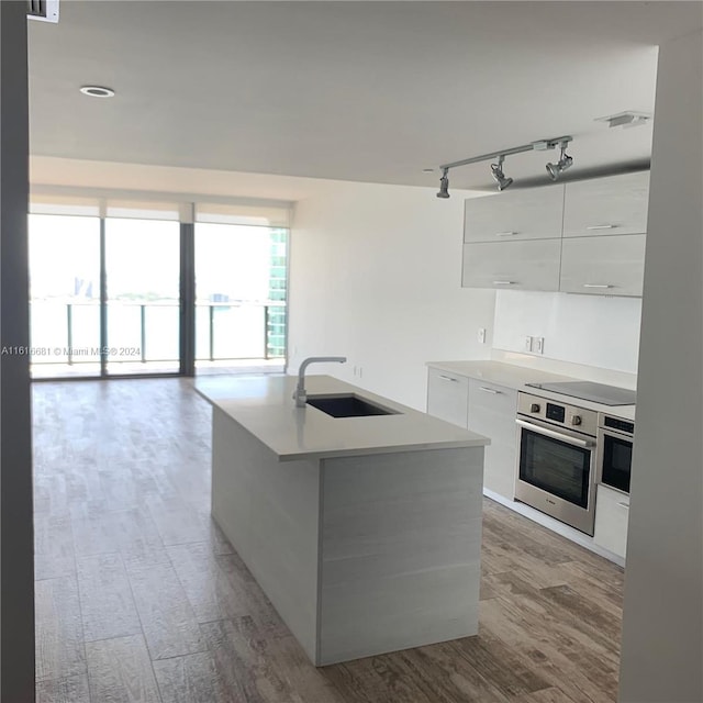 kitchen with sink, oven, white cabinets, black electric stovetop, and a center island with sink