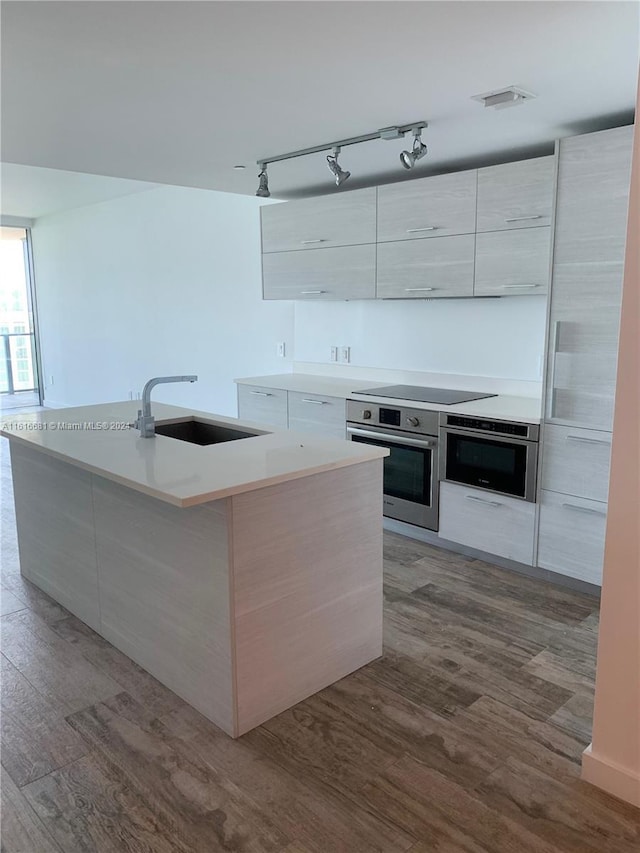kitchen featuring stainless steel oven, black electric stovetop, sink, and a kitchen island with sink