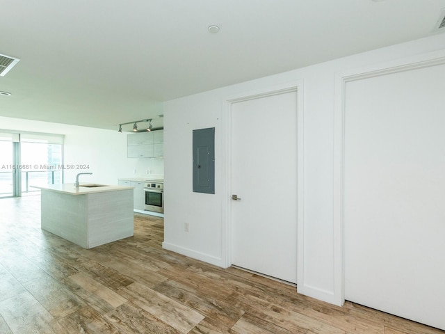 kitchen featuring sink, white cabinetry, stainless steel oven, electric panel, and an island with sink