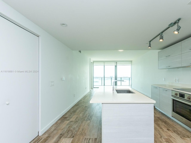 kitchen with sink, a center island, track lighting, stainless steel oven, and light wood-type flooring