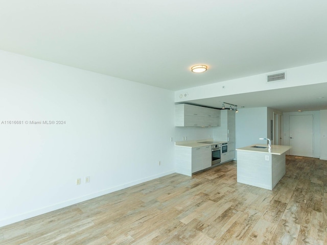 kitchen with sink, light hardwood / wood-style flooring, white cabinets, a center island with sink, and stainless steel oven