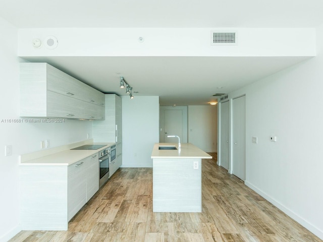 kitchen featuring sink, rail lighting, black electric stovetop, light hardwood / wood-style floors, and stainless steel oven