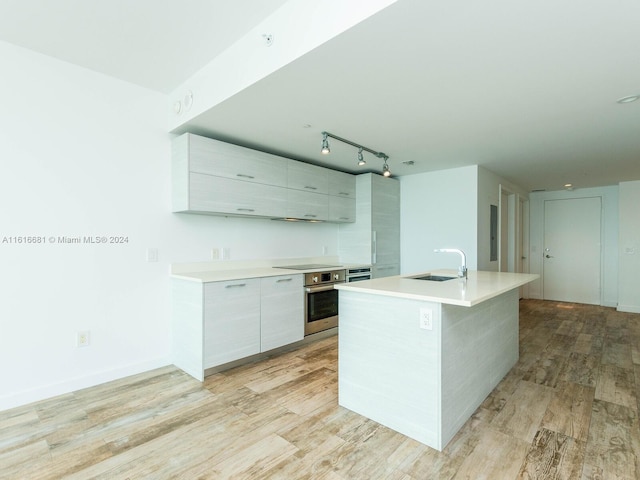 kitchen with sink, stainless steel oven, a center island with sink, light wood-type flooring, and black electric cooktop