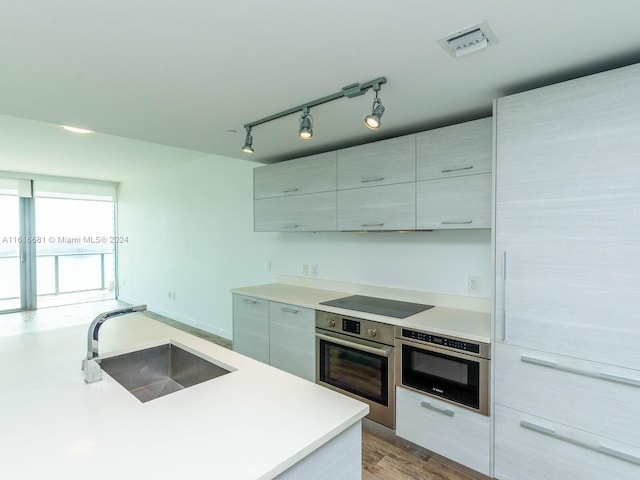 kitchen featuring sink, wall oven, black electric stovetop, track lighting, and oven