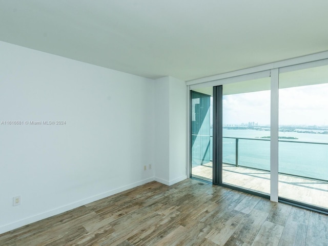 spare room with expansive windows, a water view, and hardwood / wood-style floors