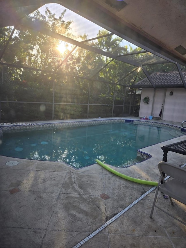 pool at dusk featuring glass enclosure, a patio area, and an outbuilding