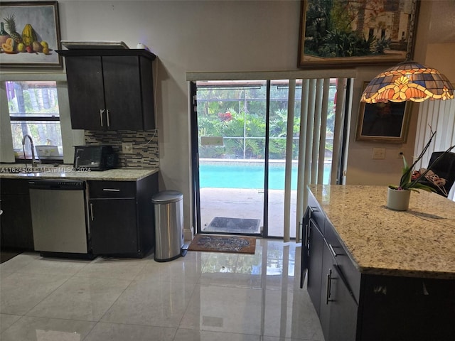 kitchen featuring backsplash, light stone counters, stainless steel dishwasher, and sink