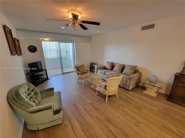 living room with light wood-type flooring, ceiling fan, and a textured ceiling