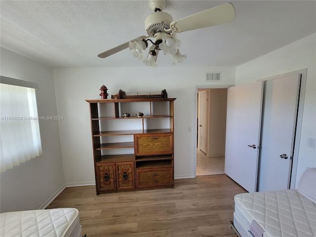 bedroom with ceiling fan, a textured ceiling, and light wood-type flooring