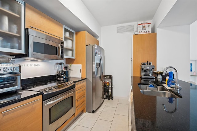 kitchen with appliances with stainless steel finishes, light tile patterned floors, dark stone counters, and sink