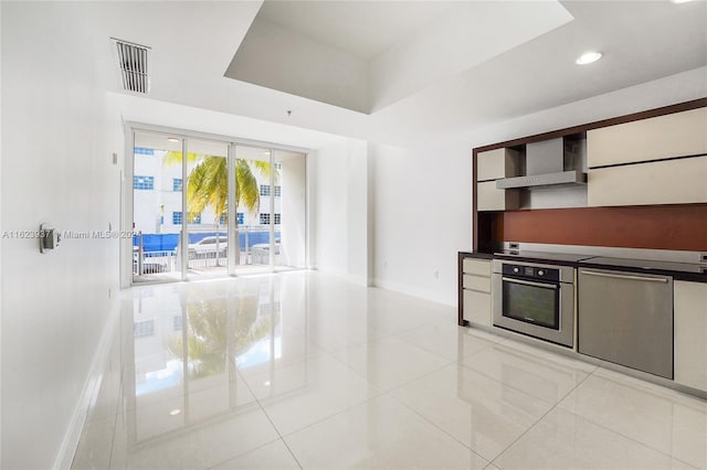 kitchen with stainless steel oven, light tile patterned floors, and wall chimney range hood