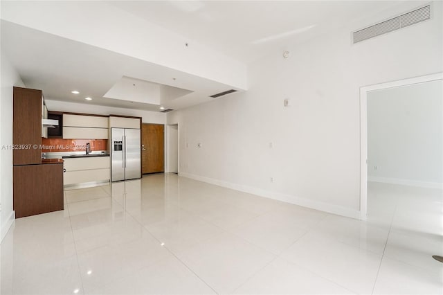 unfurnished living room with sink, a raised ceiling, and light tile patterned flooring