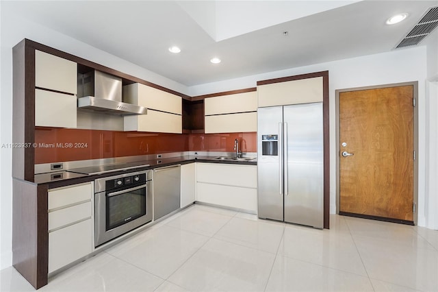 kitchen with appliances with stainless steel finishes, white cabinetry, wall chimney range hood, sink, and light tile patterned floors