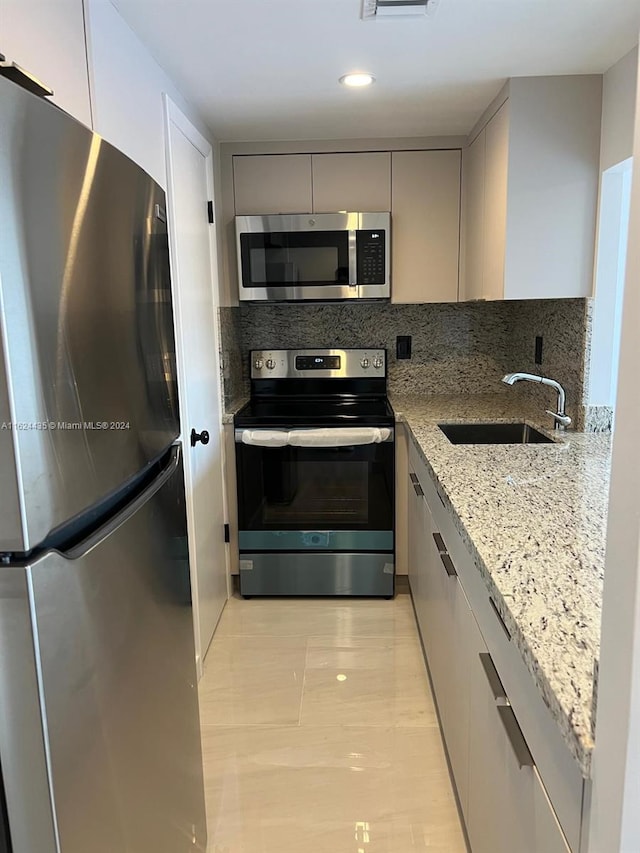 kitchen with appliances with stainless steel finishes, tasteful backsplash, gray cabinetry, sink, and light stone counters