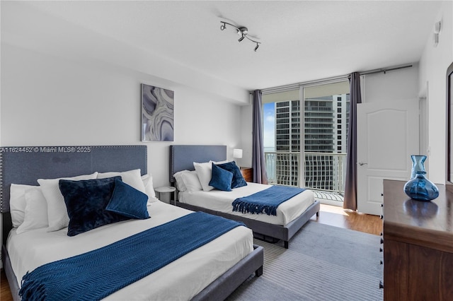 bedroom with rail lighting, hardwood / wood-style floors, access to exterior, and expansive windows