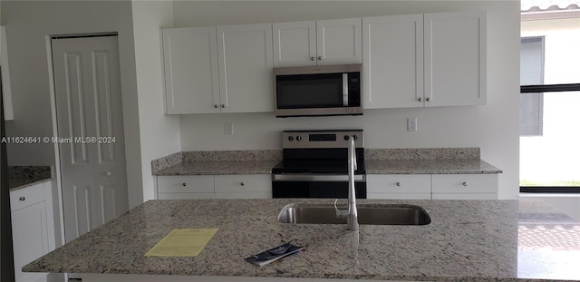 kitchen featuring appliances with stainless steel finishes, white cabinets, light stone countertops, and sink