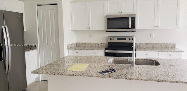 kitchen featuring appliances with stainless steel finishes, white cabinets, sink, light tile patterned floors, and light stone countertops