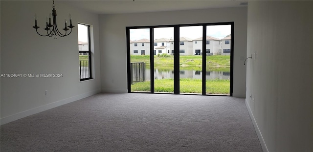 empty room featuring a water view, carpet, a chandelier, and a wealth of natural light