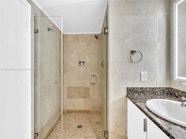 bathroom with a shower with door, crown molding, tile walls, and vanity