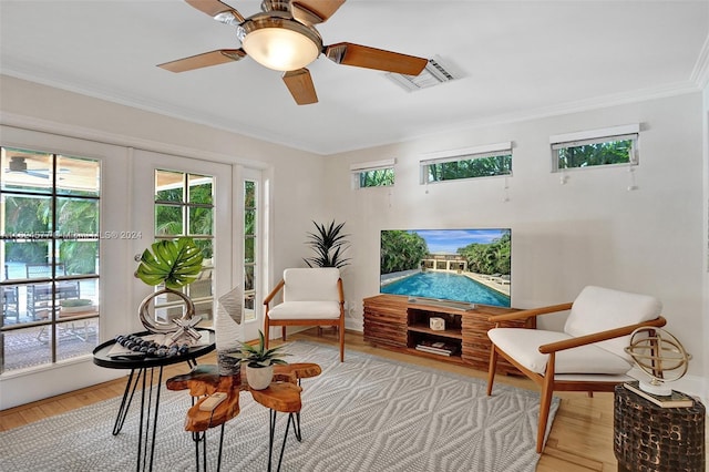 living area with ceiling fan, visible vents, light wood finished floors, and ornamental molding