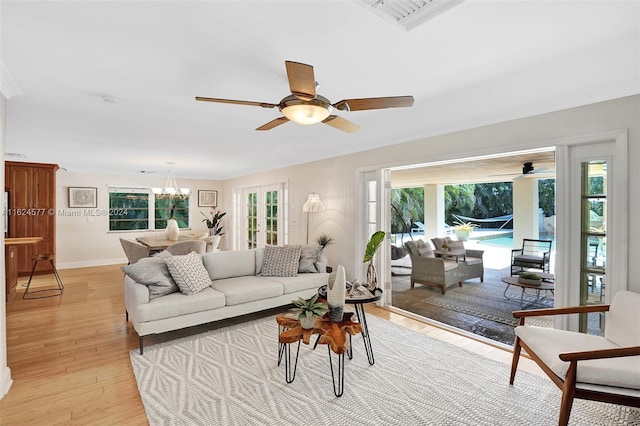 living room with ceiling fan with notable chandelier, light wood-style flooring, and baseboards
