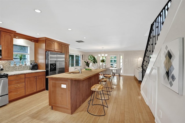 kitchen with stainless steel appliances, a sink, a center island with sink, a kitchen bar, and light wood-style floors